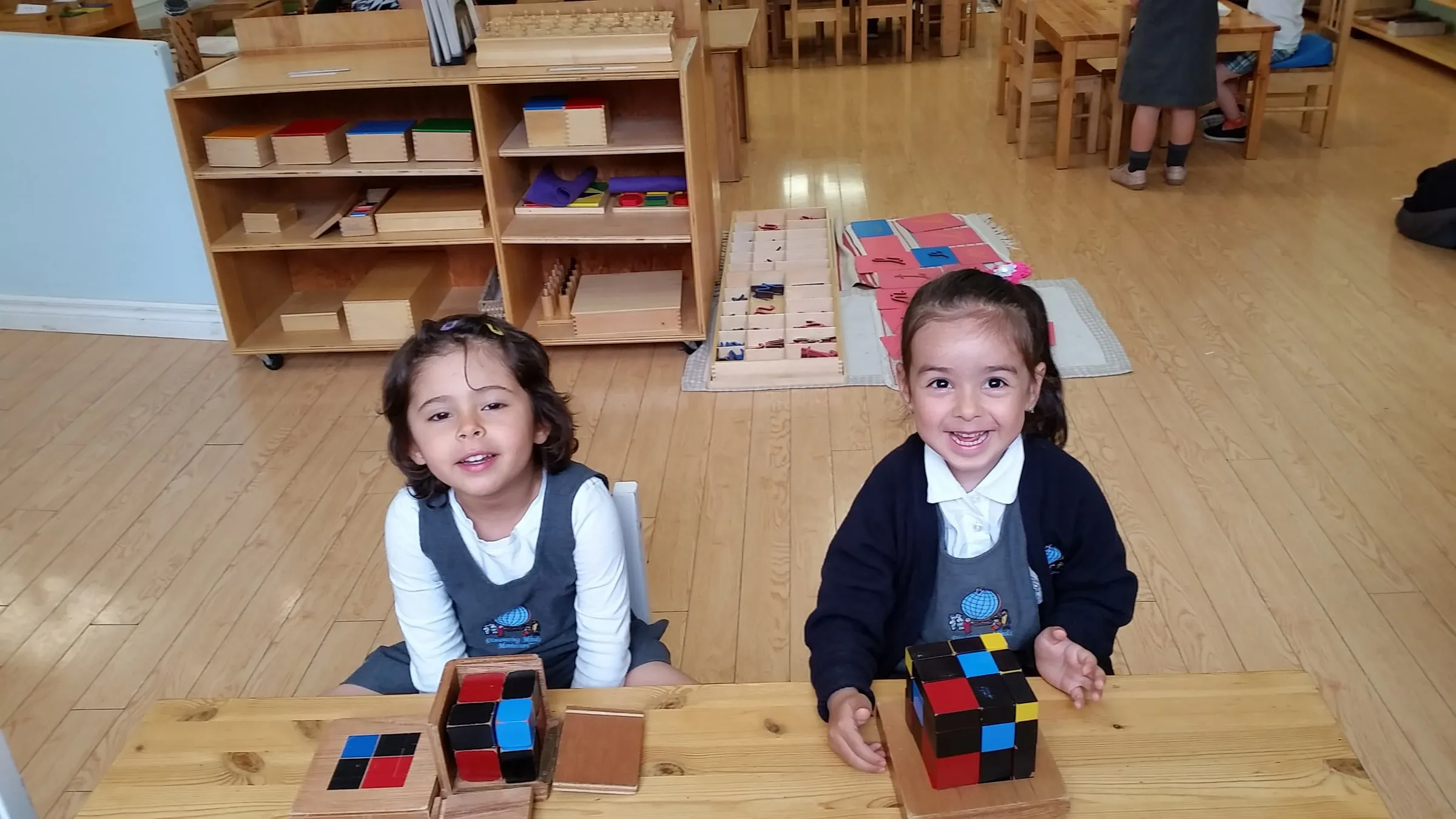 Two young girls smiling at a table with the Montessori binomial cube
