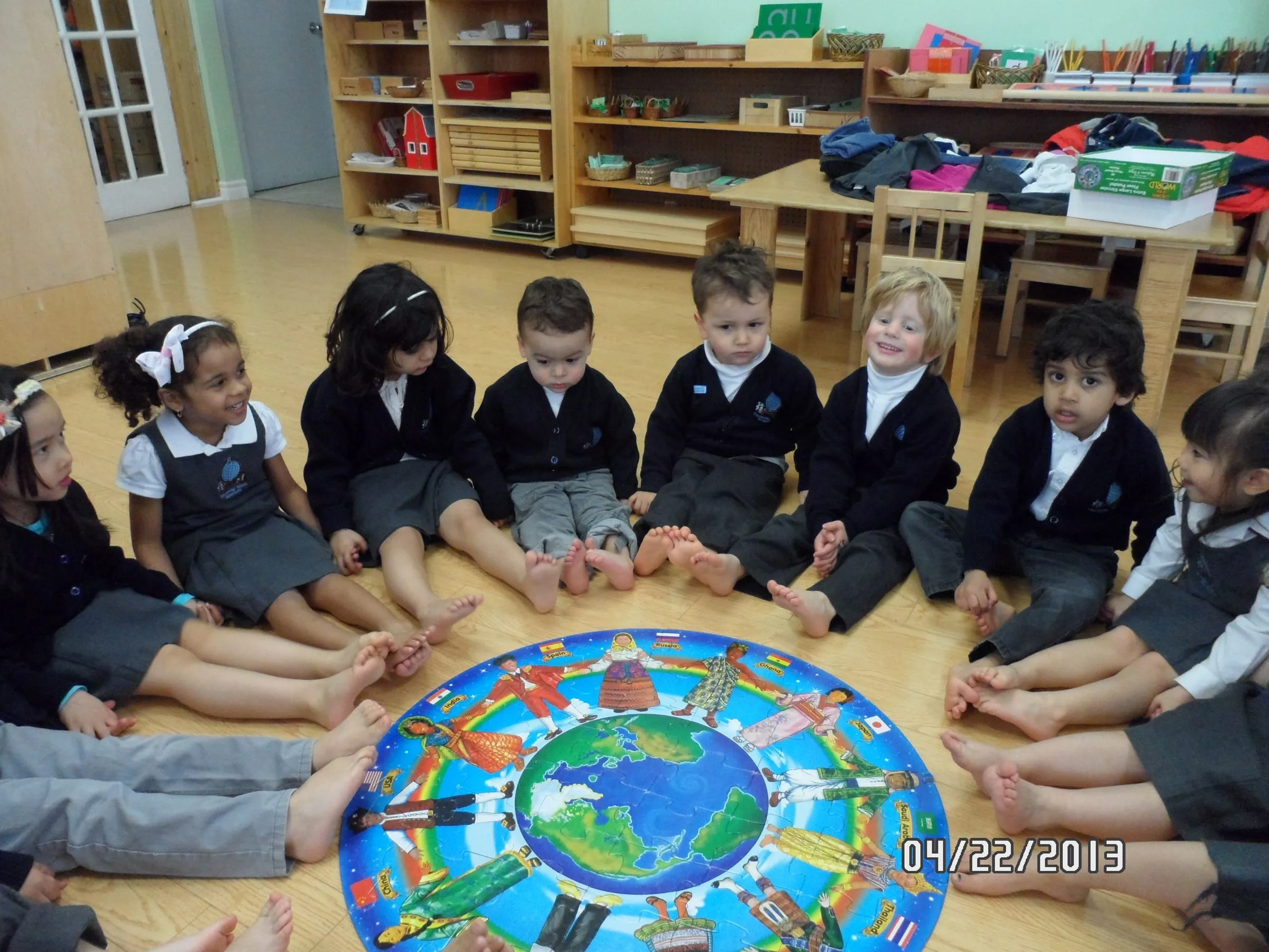 Children sitting in a circle on the classroom floor around a world map floor puzzle