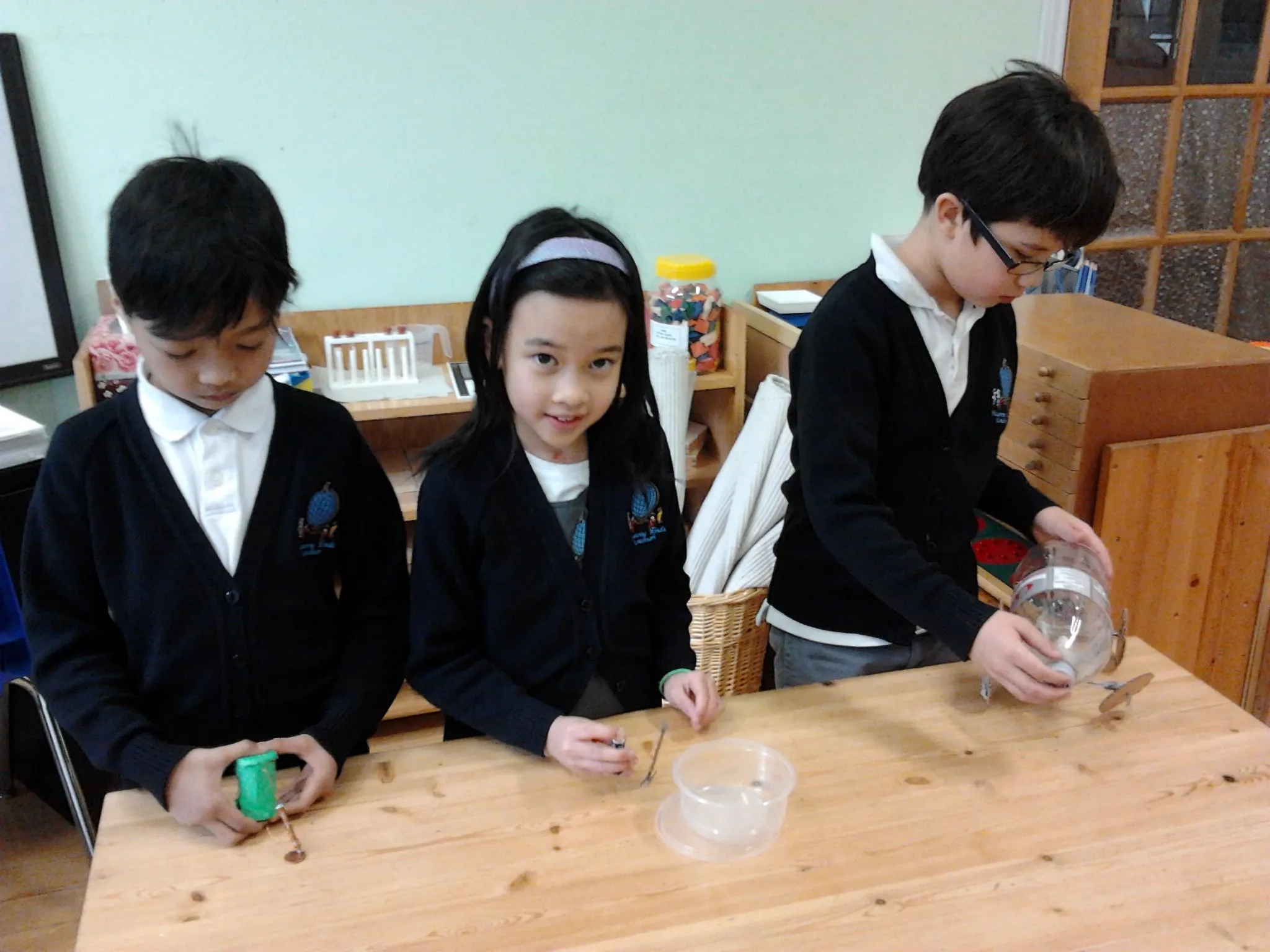 Three lower elementary students running an experiment together at a wooden classroom table