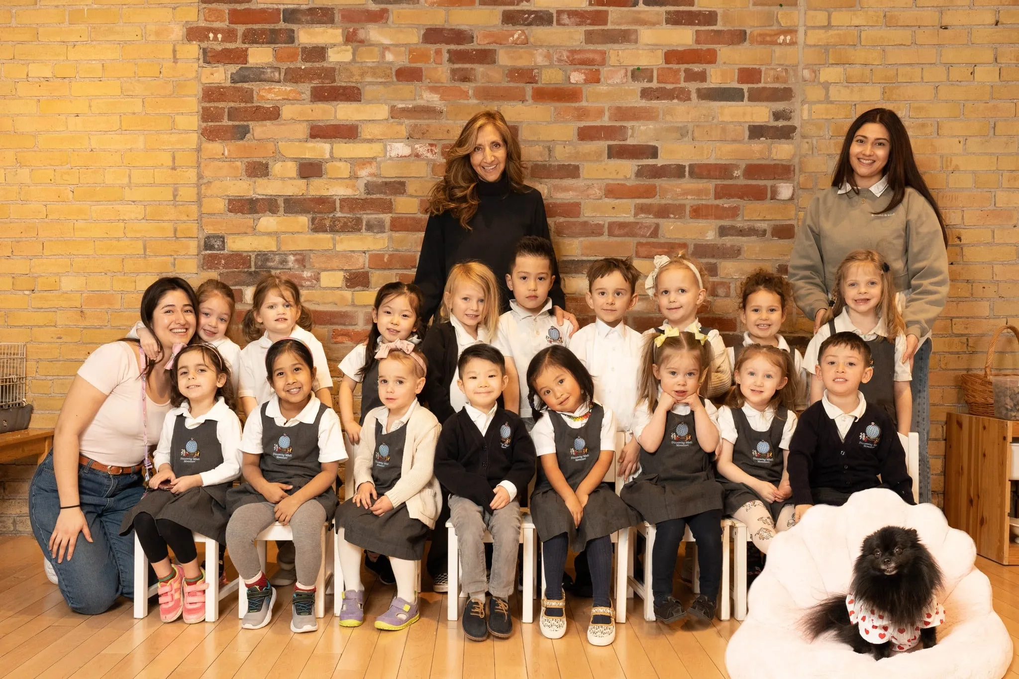 The children and staff of Discovering Minds Montessori photographed together in front of the school’s exposed brick wall