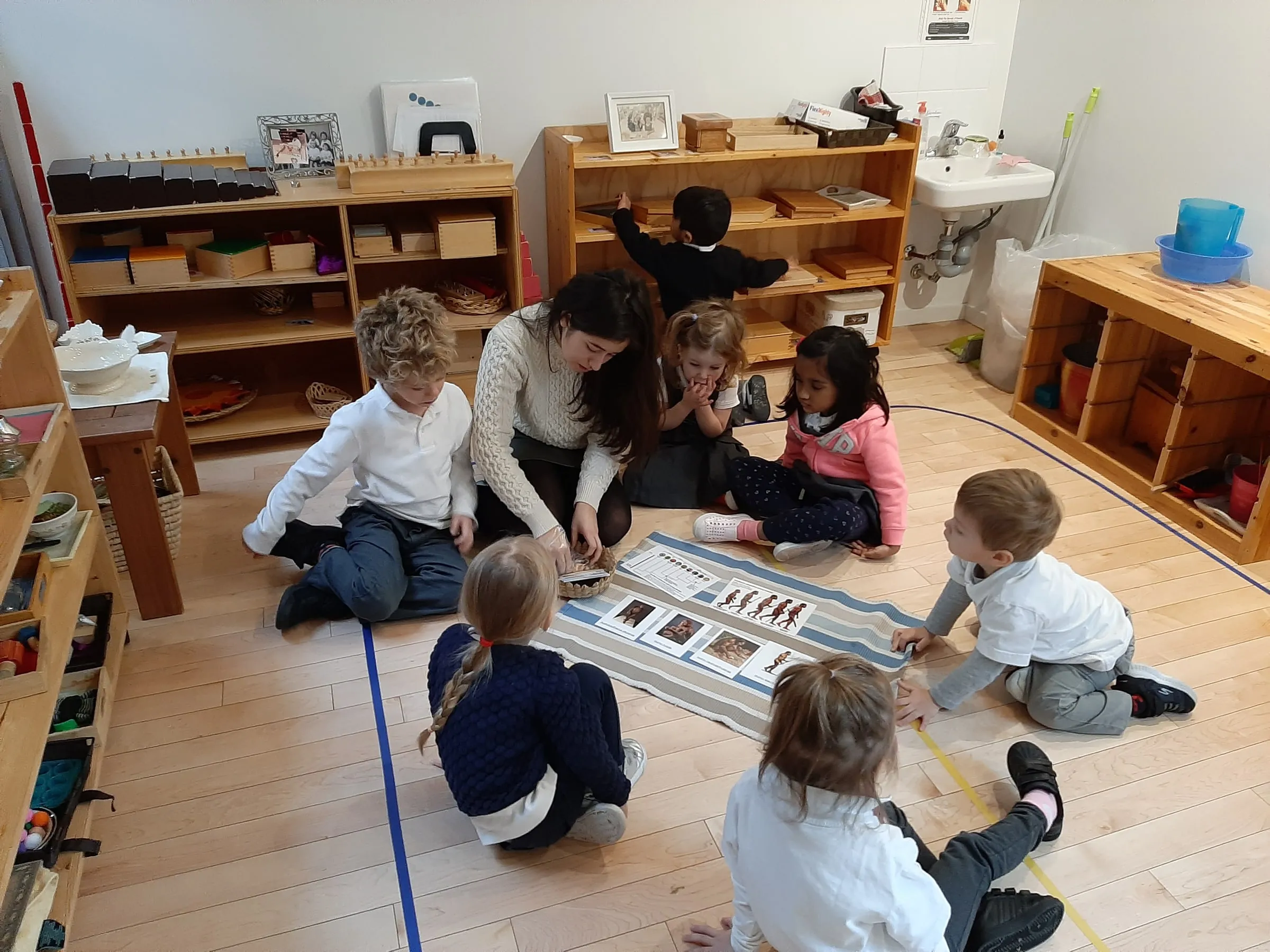 A teacher giving a lesson on a floor mat to six children gathered around her