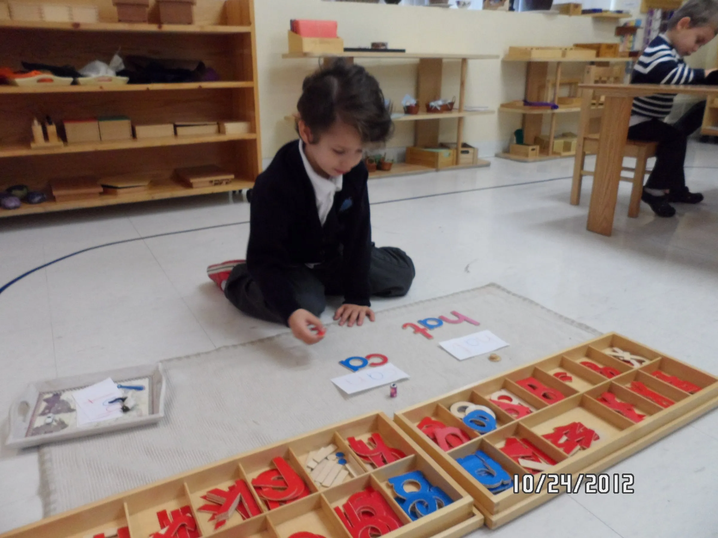 A kindergarten child building words on the floor with the Montessori movable alphabet