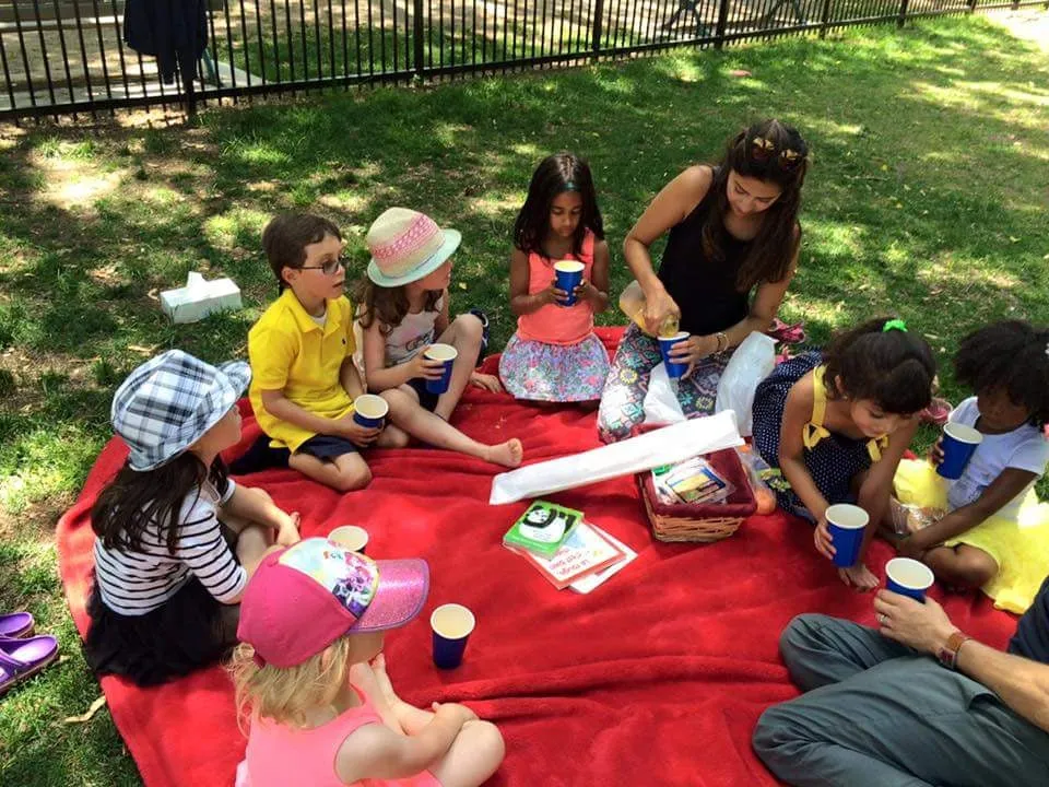 Children and teachers sitting on a blanket in a Toronto park during the summer programme